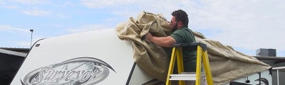 man on ladder putting cover over roof of rv. 
